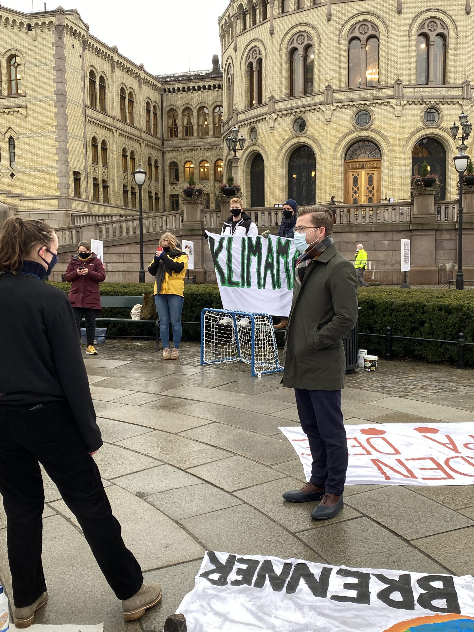 Ungdommer demonstrerer utenfor Stortinget. En mann med munnbind følger med. 