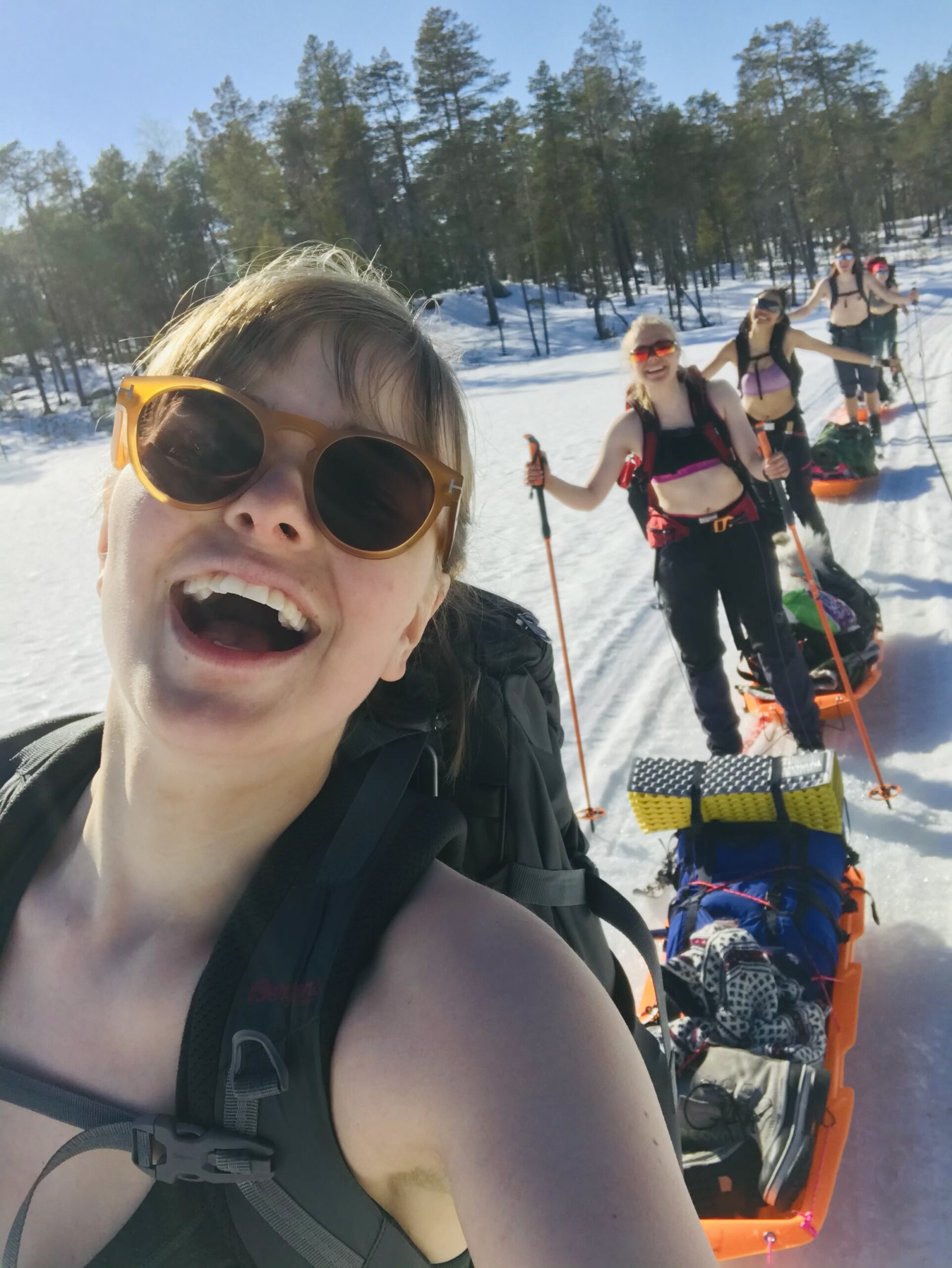 Selfie av en gruppe unge kvinner som går på ski i sola med sporstopper og pulk. 