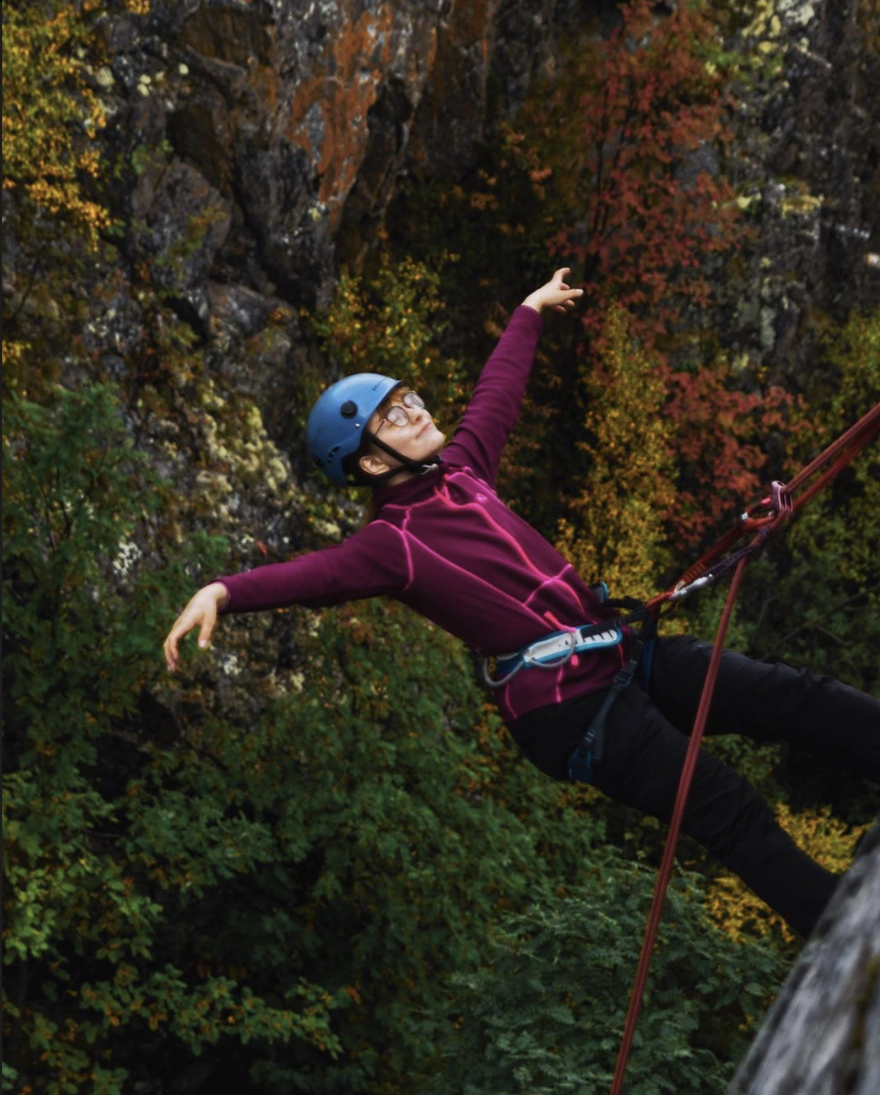 En ung kvinne holder hendene ut fra siden mens hun rappellerer ned en fjellvegg.