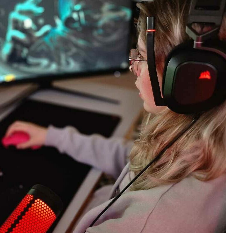 en ung kvinne sitter foran en gaming-pc med headset