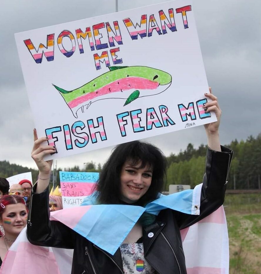 en ung kvinne i et pridetog som holder en plakat med teksten 