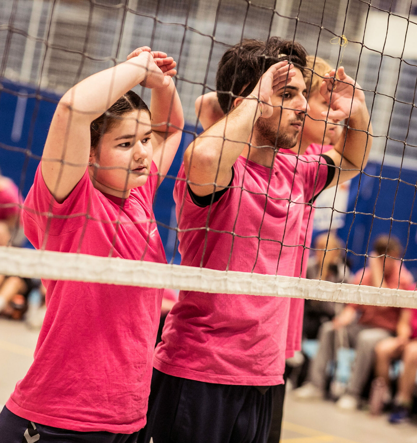 Tre personer står bak et volleyballnett med armene hevet.