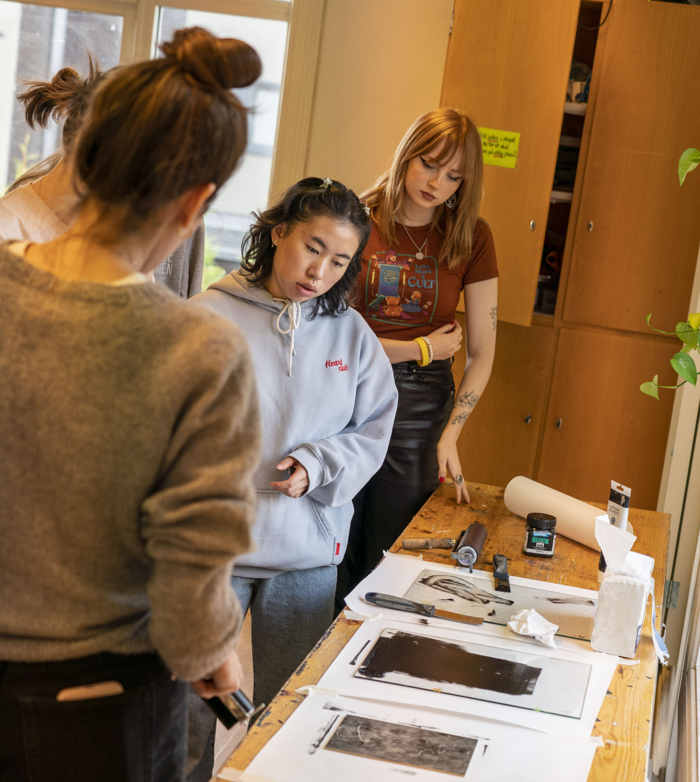 Flere unge mennesker står rundt et arbeidsbord og ser på et kunstverk 