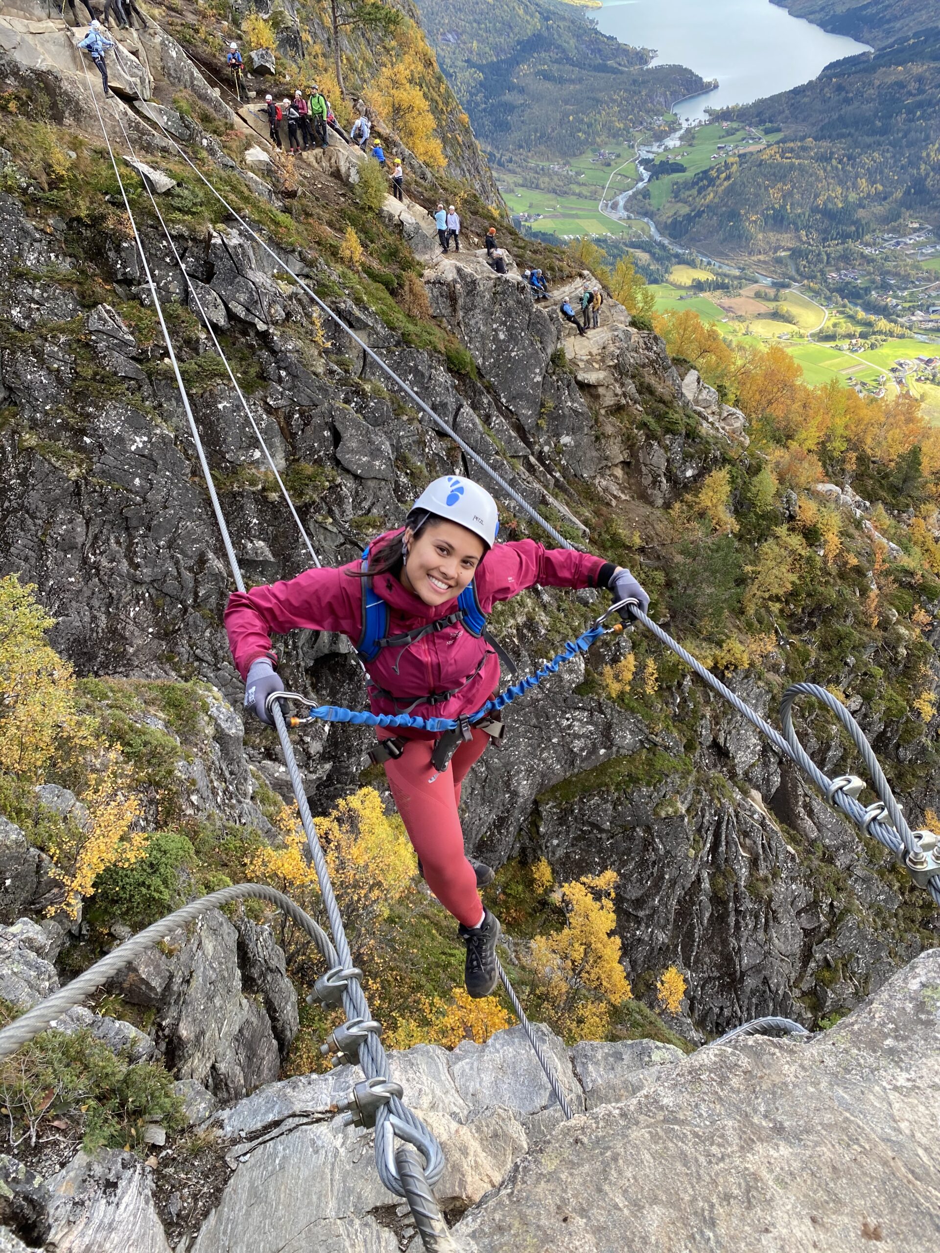 En ung jente med rosa jakke står på en hengebro over fjell. 