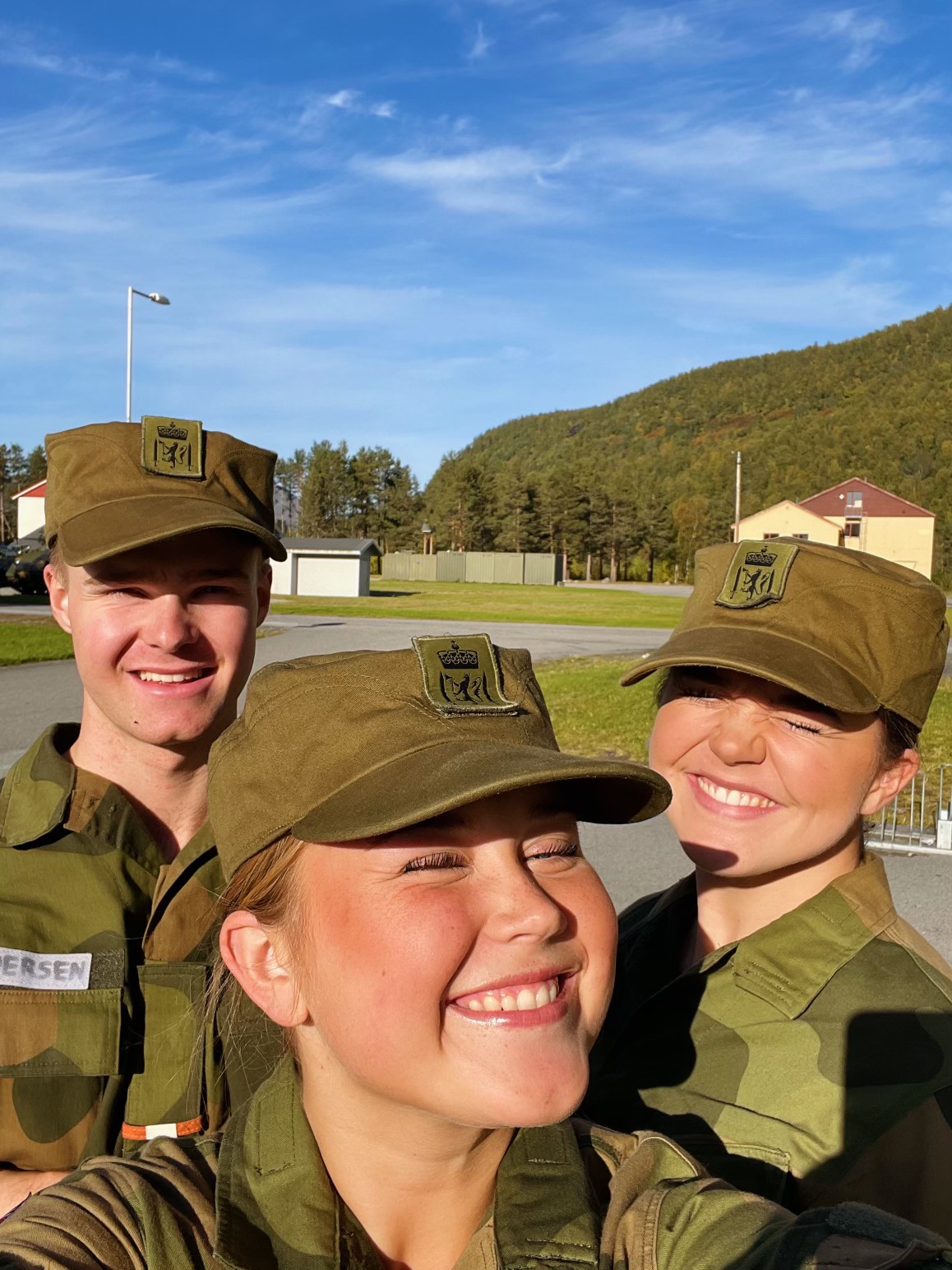 Tre ungdommer i militæruniform tar selfie i solen. 