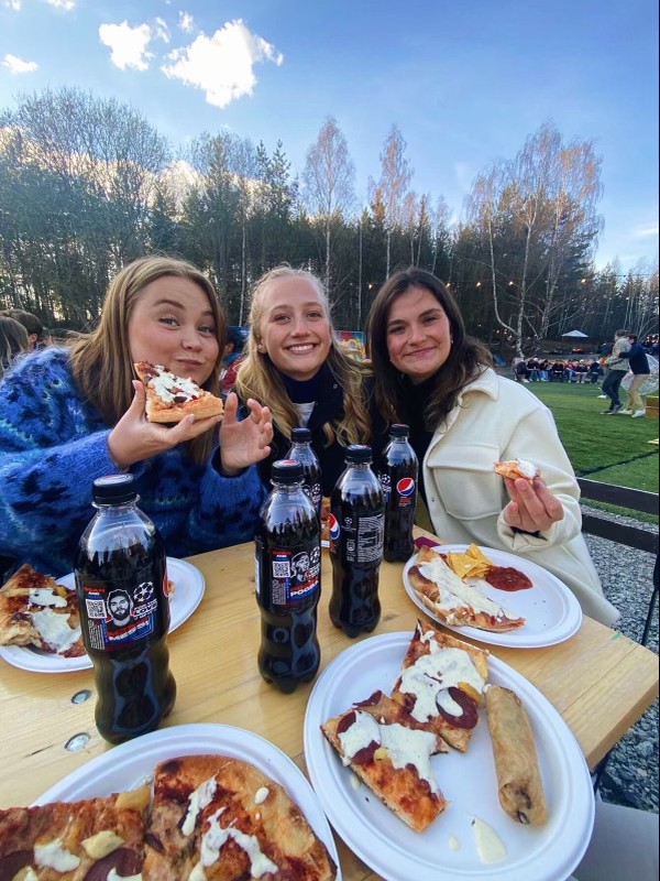 Tuva og to jenter smiler i kamera mens de spiser pizza og drikker pepsi max. 