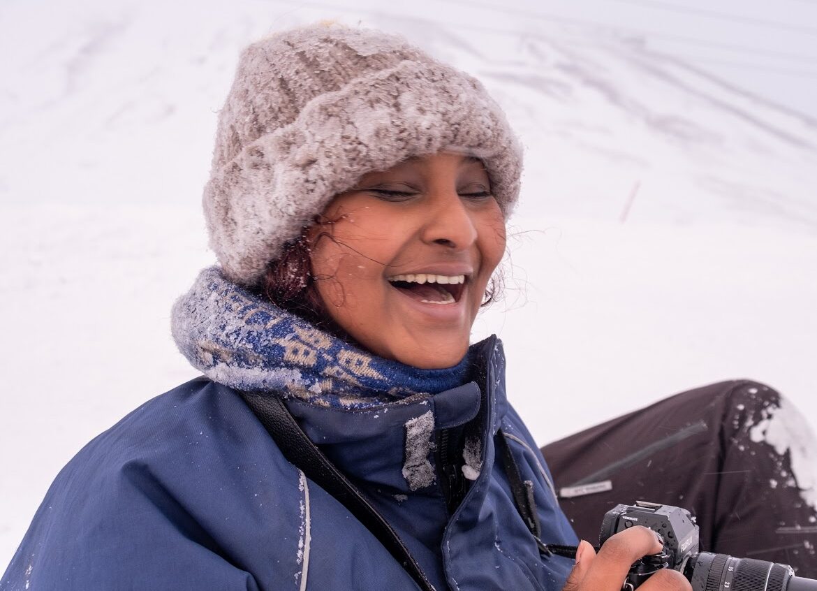 en ung kvinne med ullue tar bilder i et snødekt landskap 