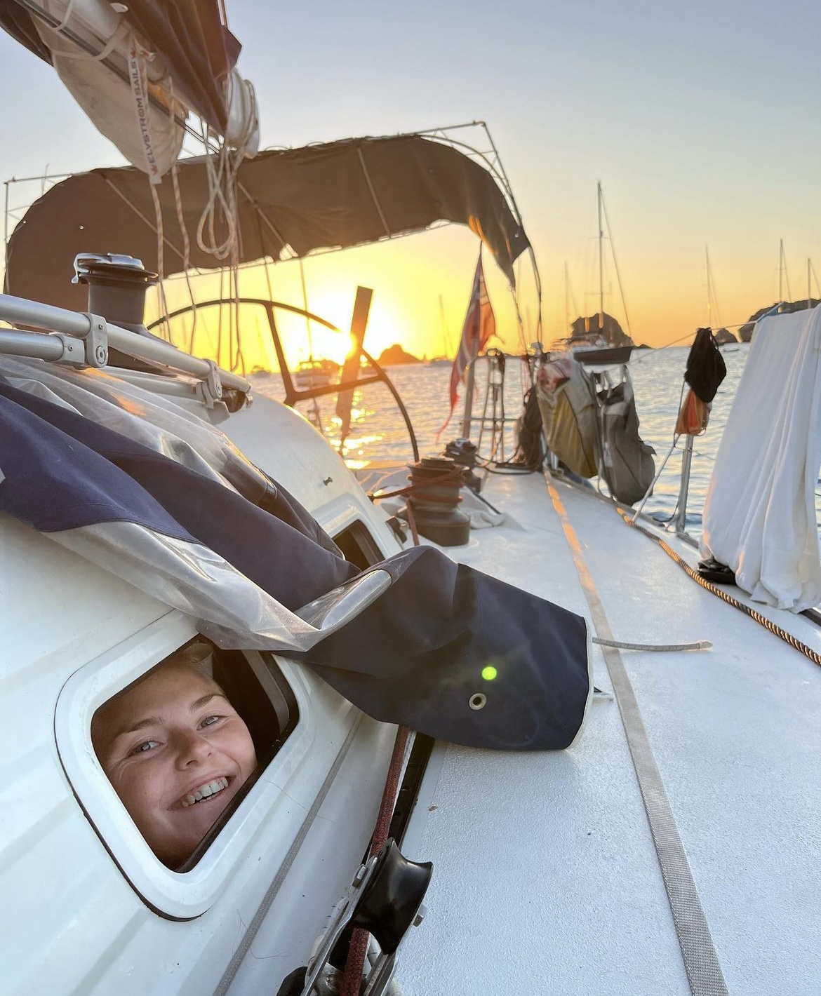 Alva kikker ut av et vindu i seilbåten i solnedgang. 