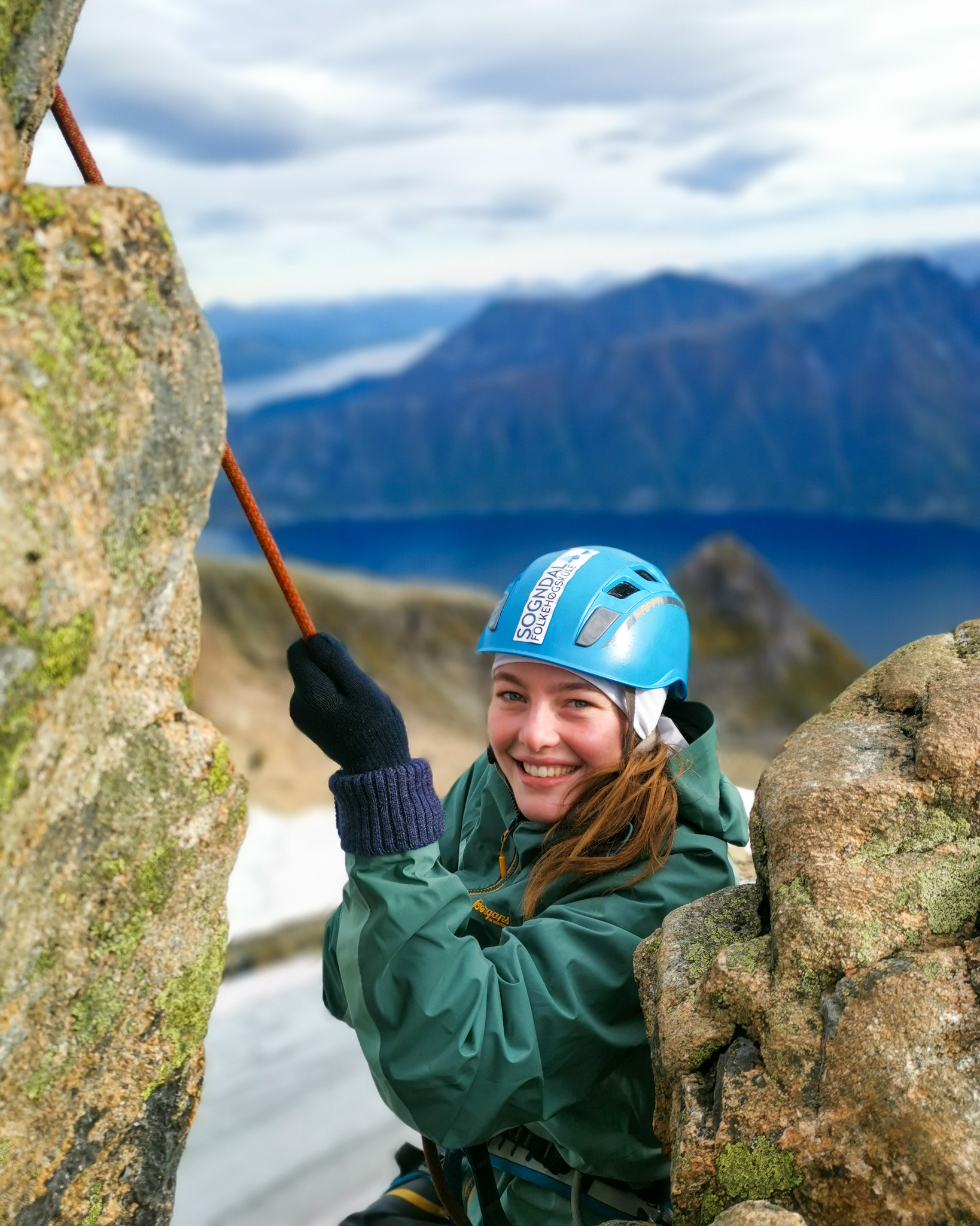 En ung kvinne henger i et klatretau i en fjellvegg