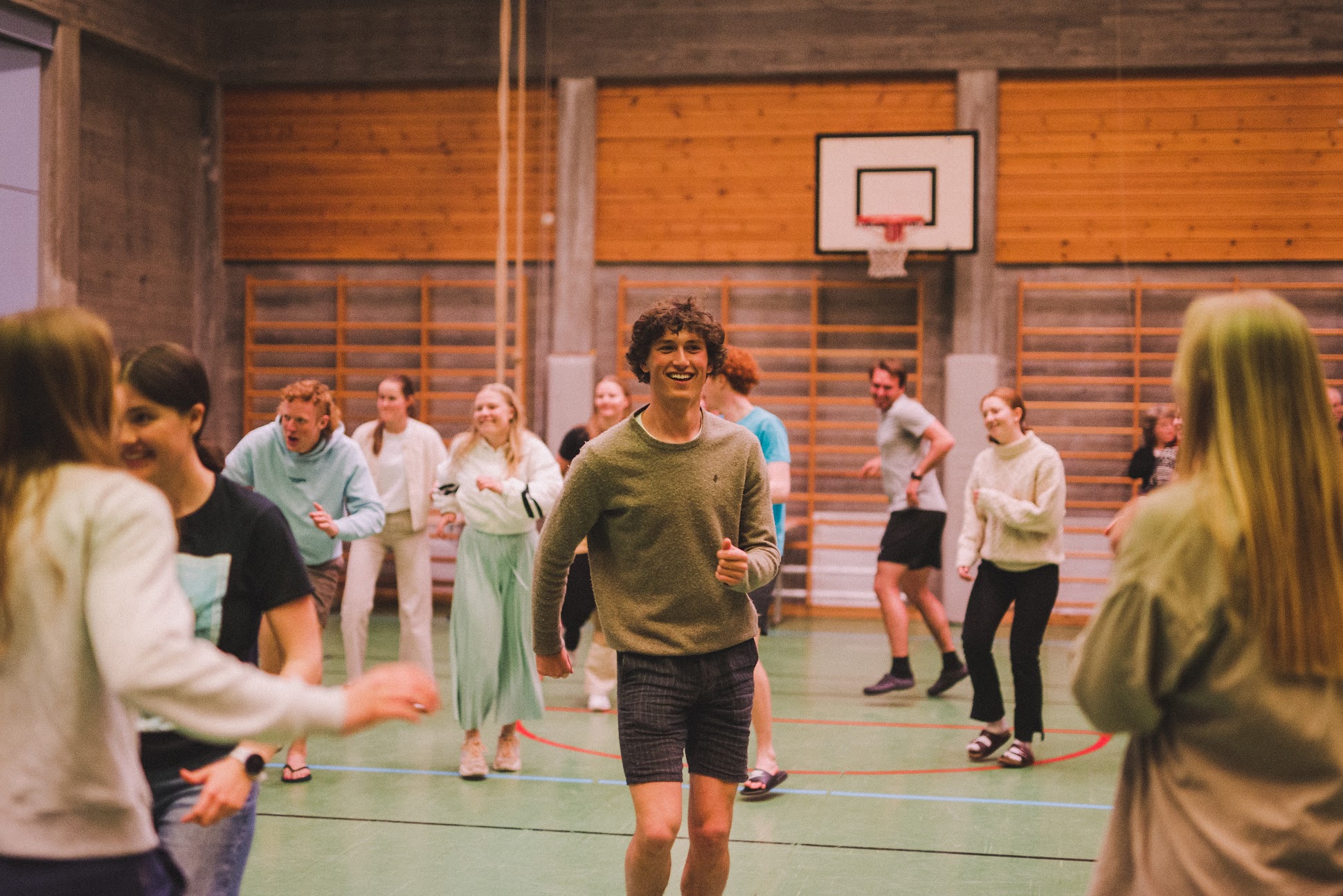 en gruppe unge mennesker i en gymsal, en ung mann i midten av bildet smiler mot kamera 