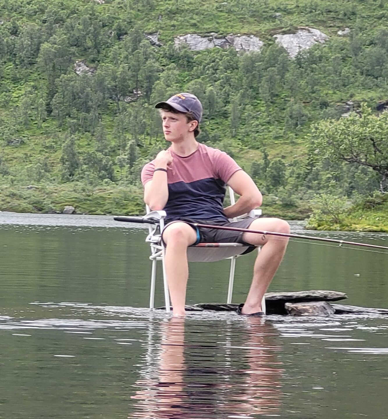 en ung mann sitter i en stol i en elv med en fiskestang på fanget 